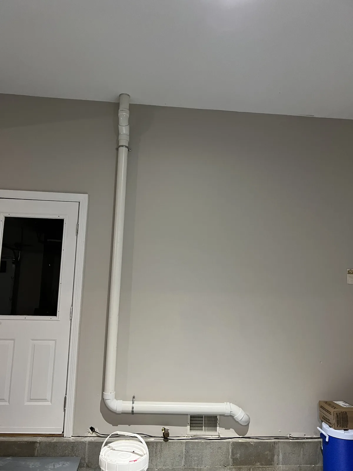 White PVC pipe running vertically along a finished lower-level wall