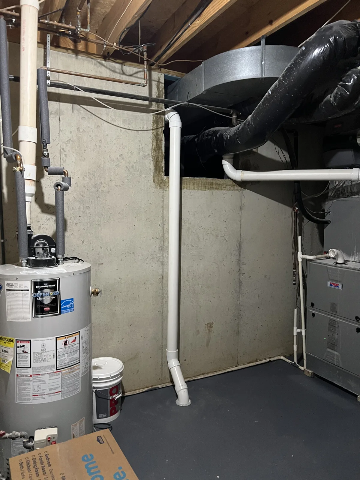 White PVC pipe installed beside a water heater and furnace in a mechanical room