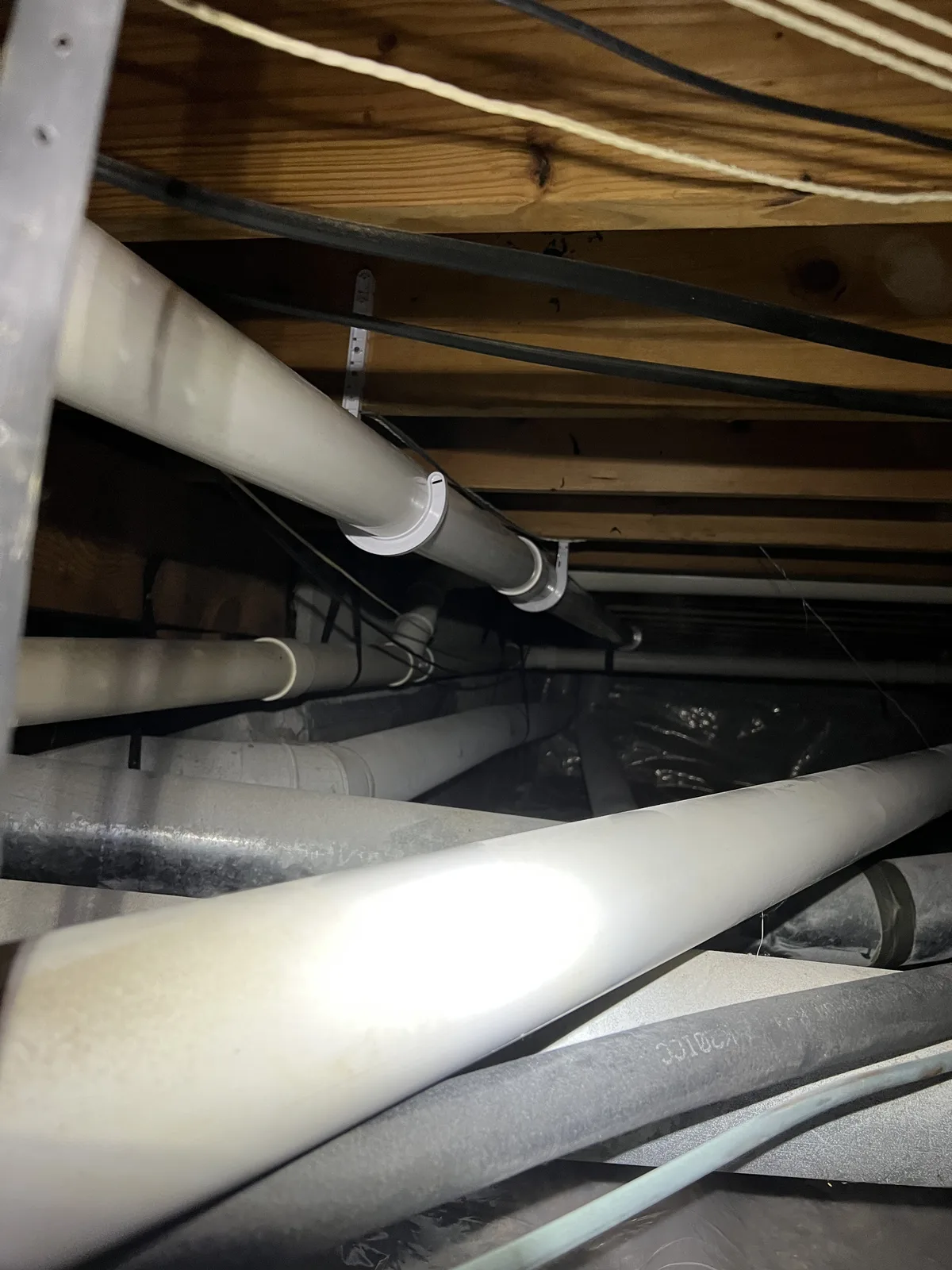 White PVC piping routed beneath a wood-framed floor with other utility lines